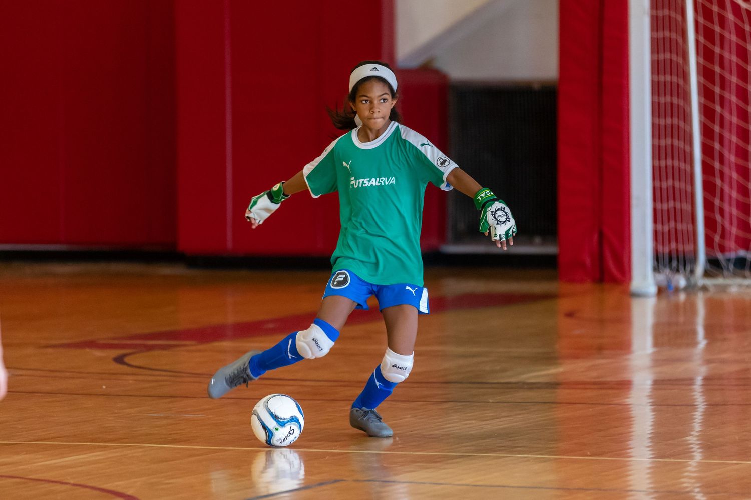 Children playing indoor soccer with one player in blue uniform preparing to kick.