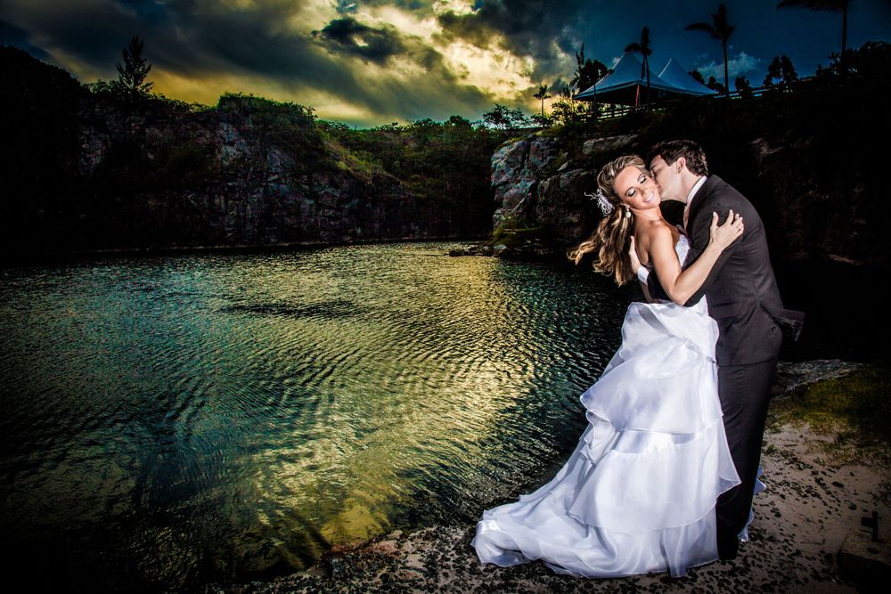 Wedding couple embracing by lake during dramatic golden hour sunset.