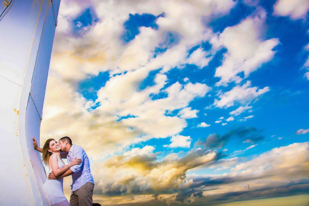 Wedding couple silhouetted against vibrant blue sky with puffy white clouds.