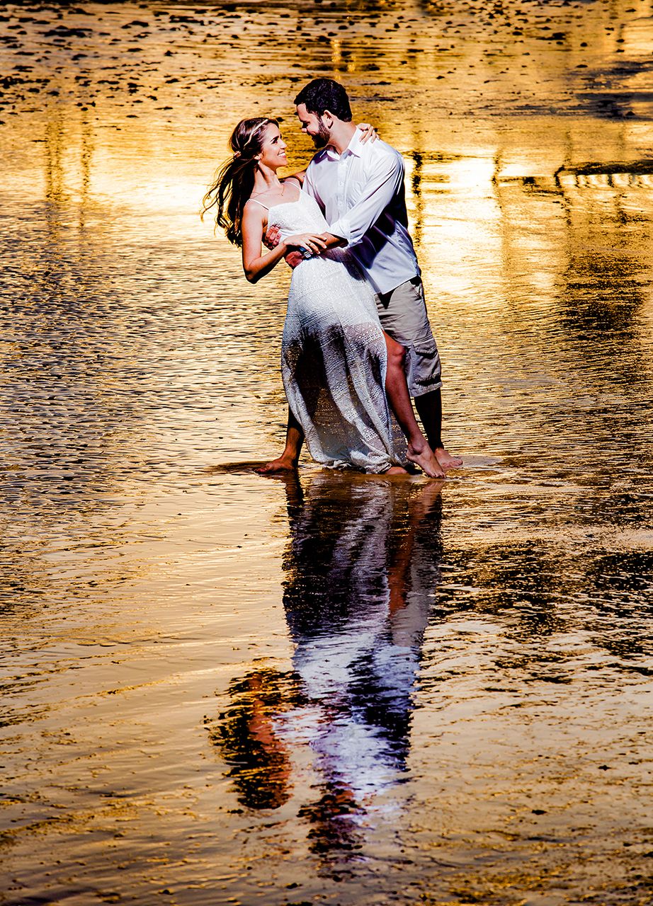 Romantic couple standing in reflective water during golden sunset creating dreamy silhouettes.