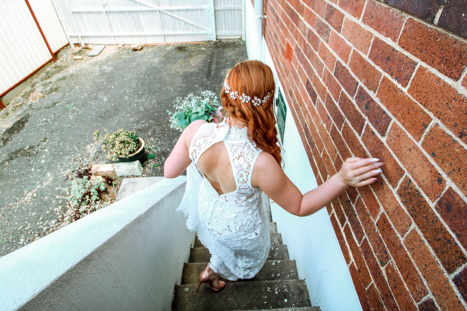 Back view of a lace wedding dress as person descends brick staircase.