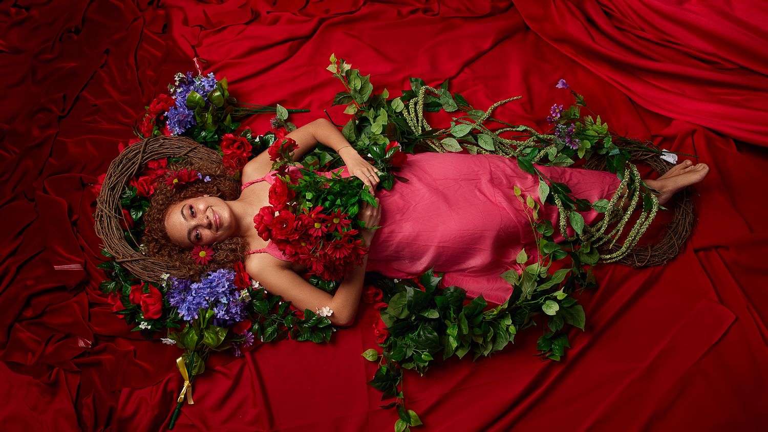 Artistic portrait with flowers and greenery on red velvet backdrop.