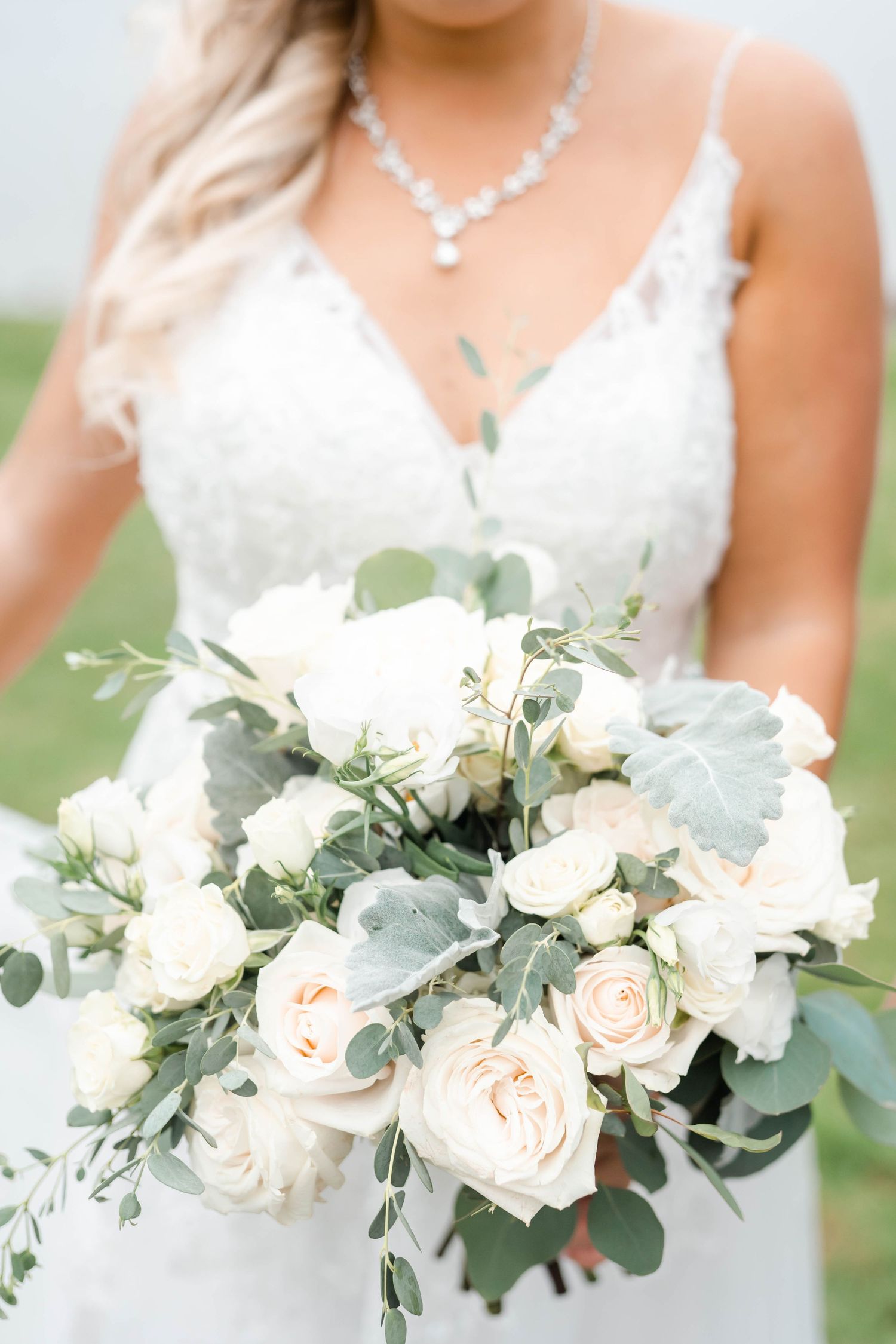 A bride holds a beautiful bouquet of white flowers and greenery.