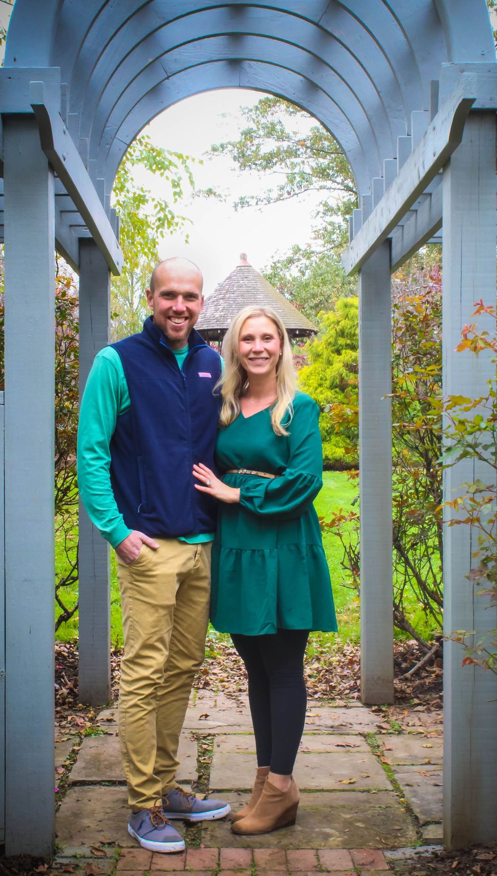 A couple in coordinating outfits poses under a blue arched garden pergola.