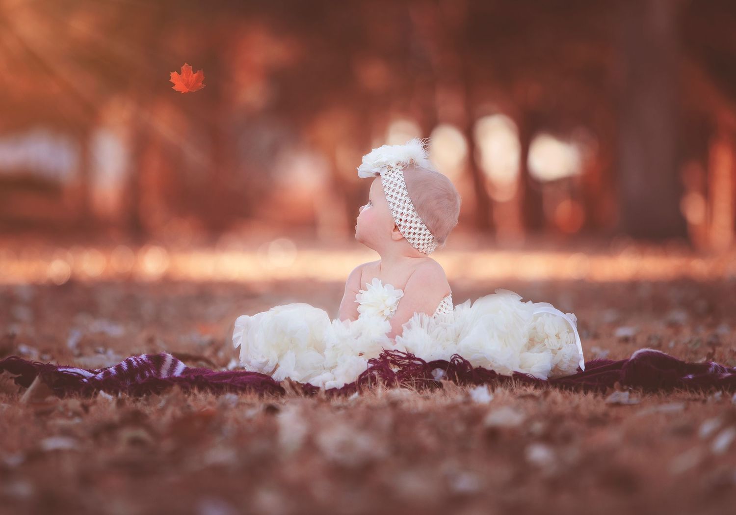 Baby in white tutu and bow in yard with leaves