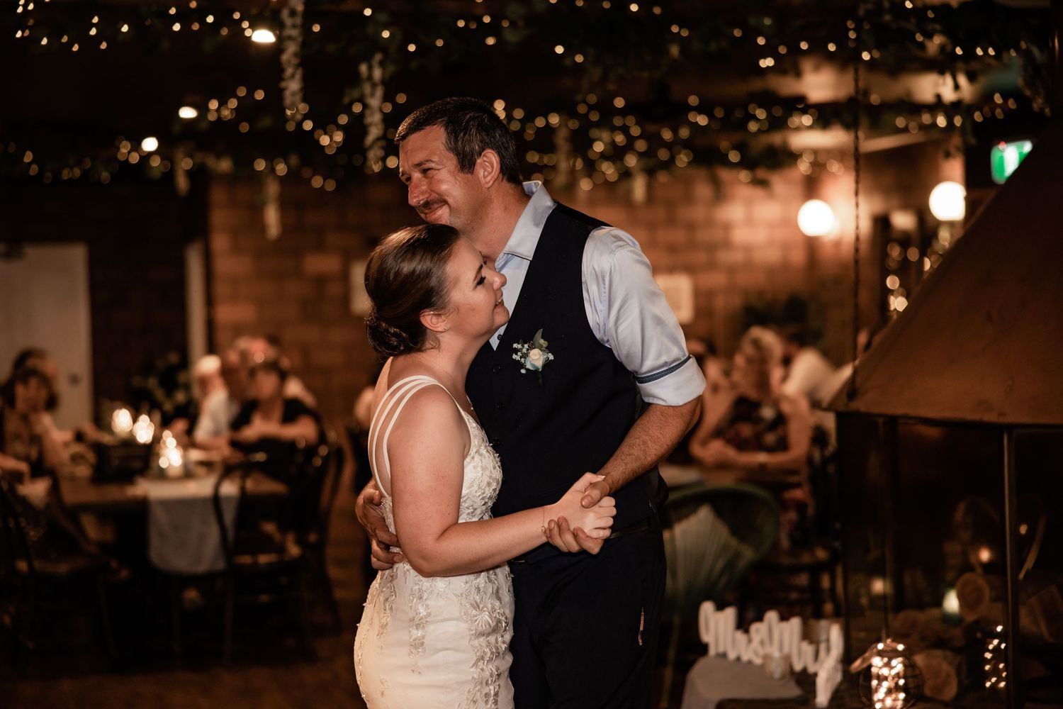 Couple shares an intimate first dance under romantic lighting at indoor wedding reception.