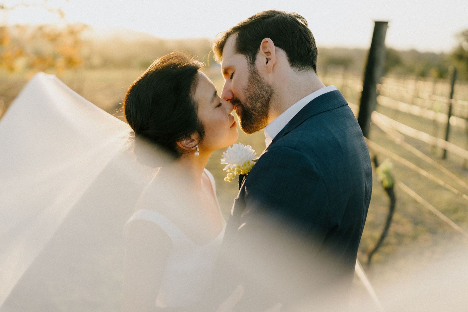 Bride and groom share a kiss, accentuated by a stunning veil shot, adding elegance to the scene at Albert River Winery