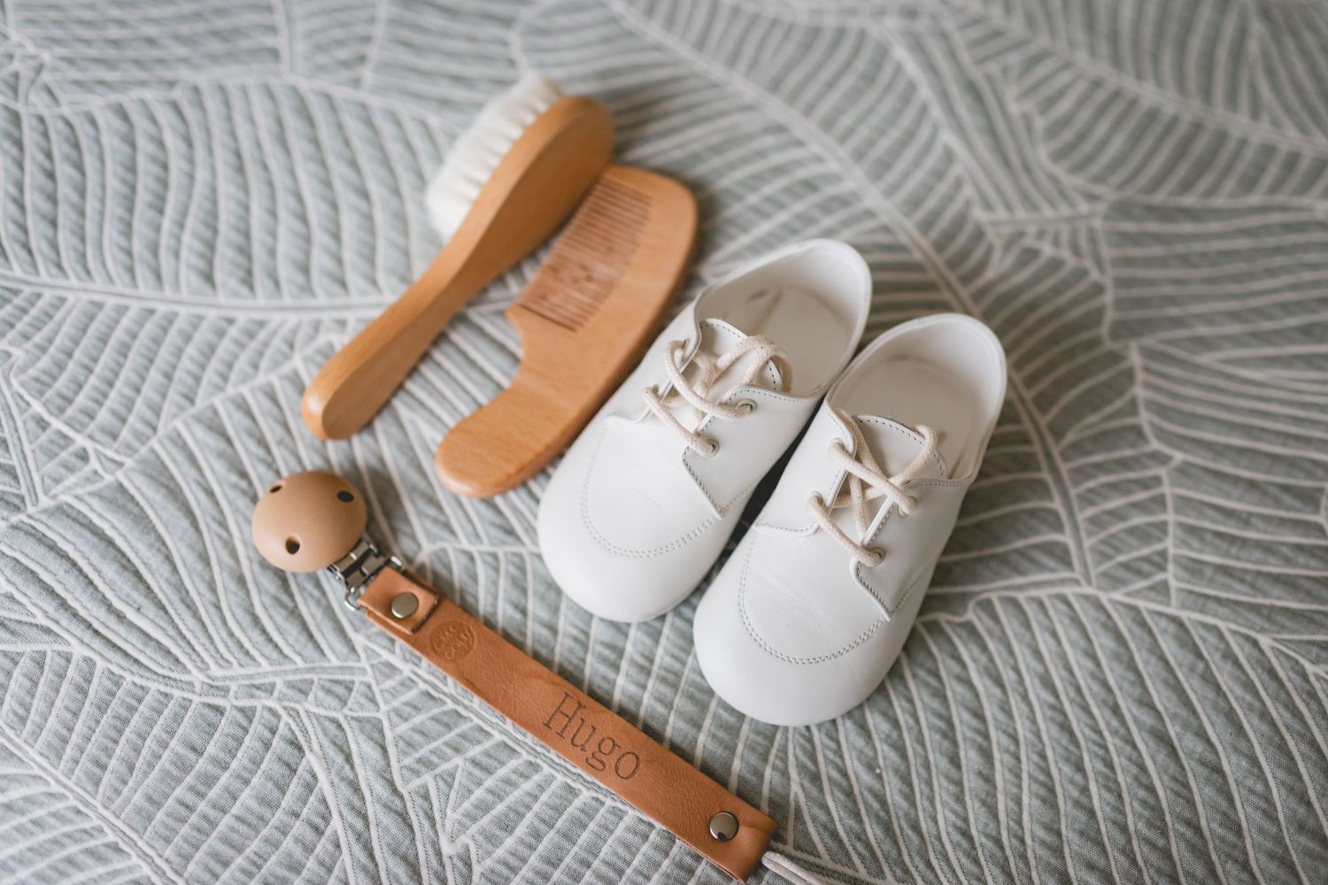 White baby shoes and wooden brush arranged on gray textured fabric.