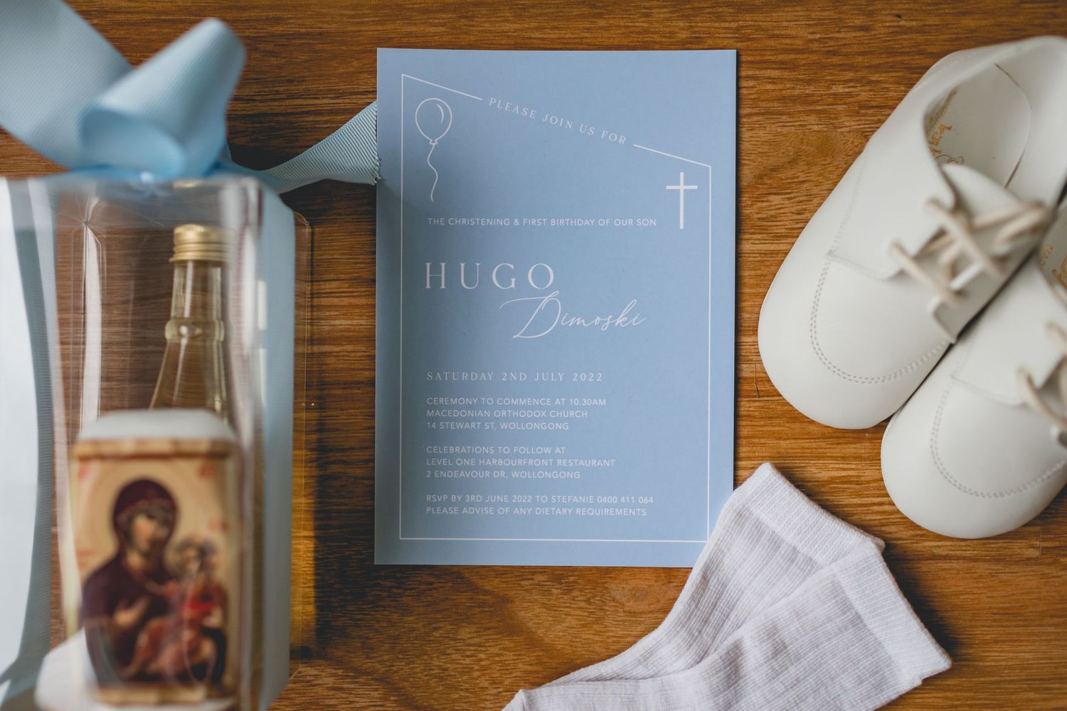 Religious baptism invitation with blue design next to baby shoes and decorative items.