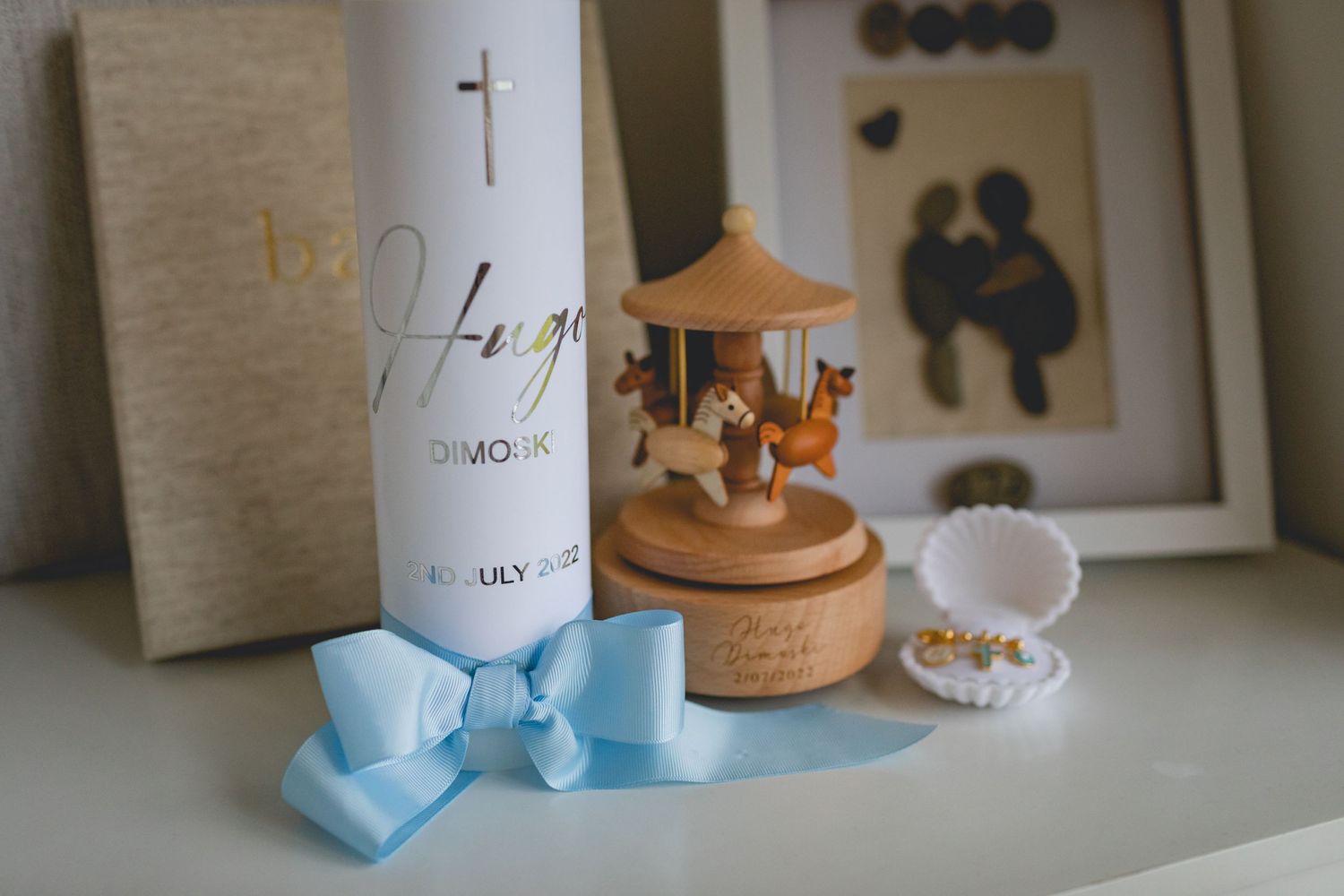 Baptism decorations including a candle with blue bow and wooden carousel on a white shelf.