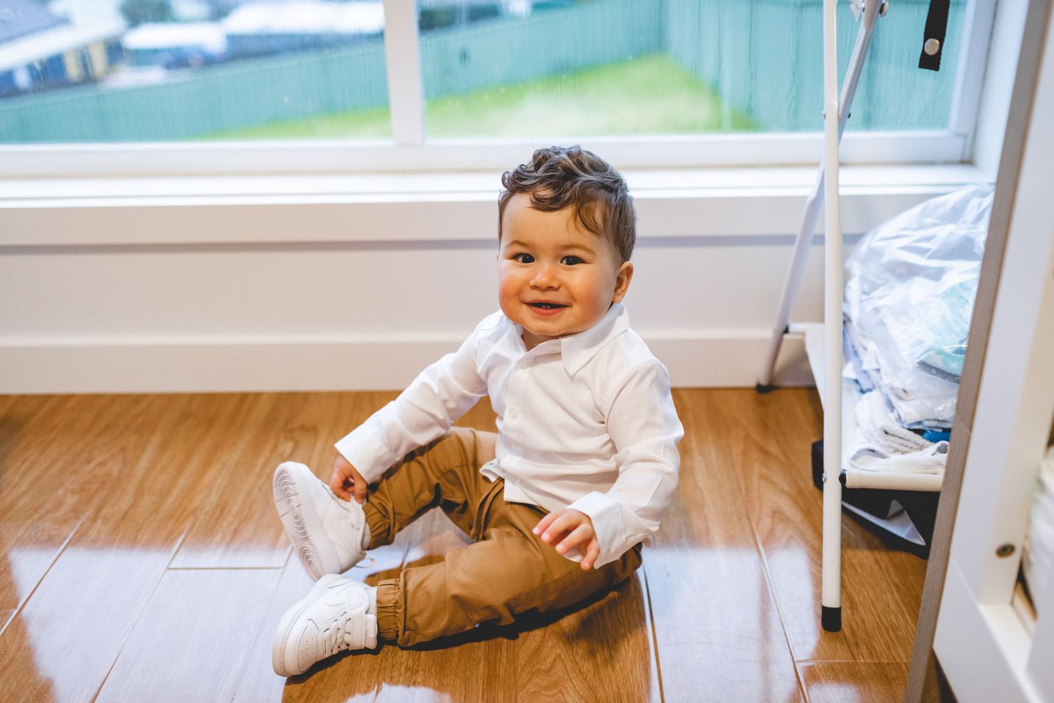 A happy child sitting on hardwood flooring in white clothing.