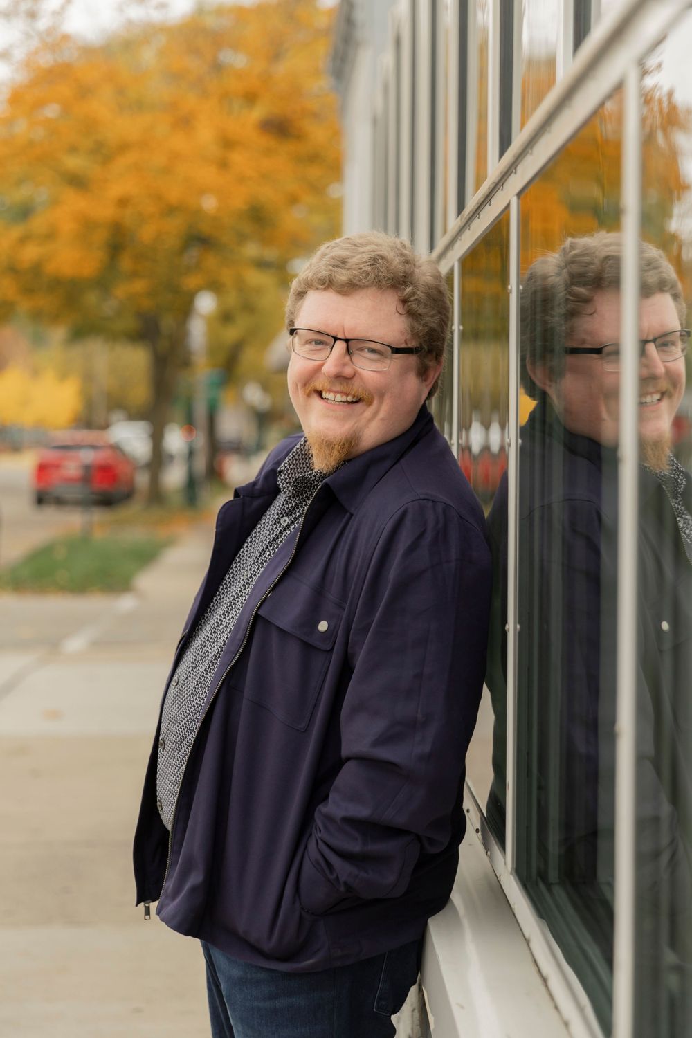 man in glasses leaning on a glass building in downtown Rochester michigan
