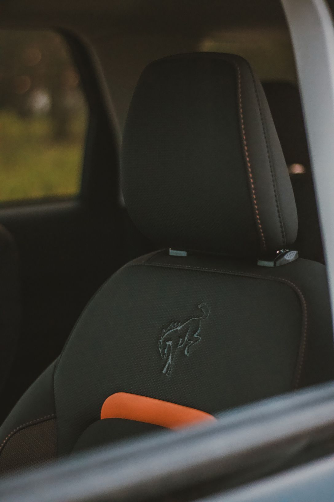 Black leather car seat with embroidered logo and orange accent detail.