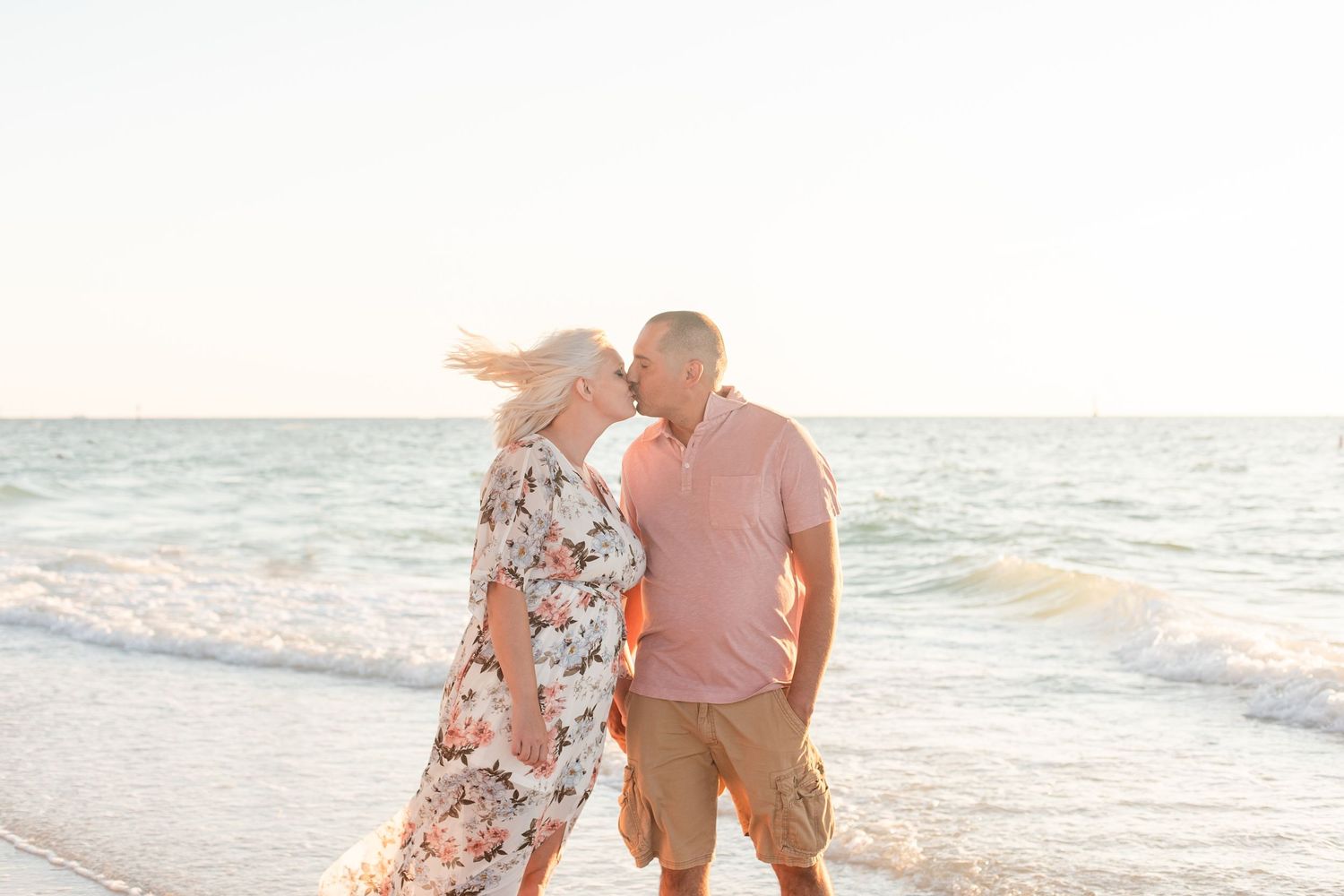 Couple embracing on a beach with waves and soft lighting in the background.