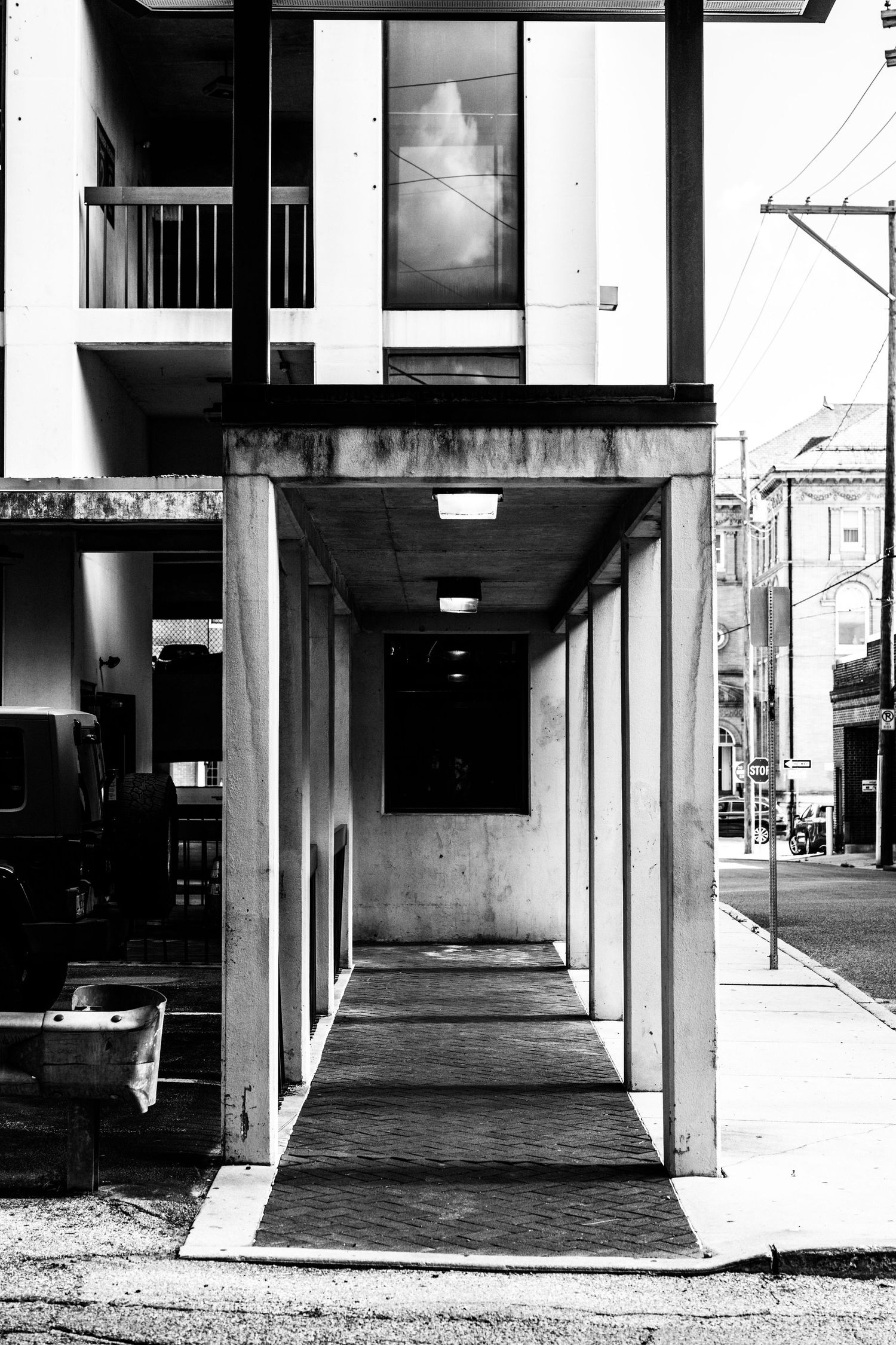 Black and white architectural photo of a covered walkway with strong geometric lines and deep shadows.