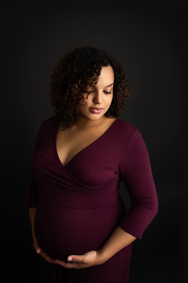 Pregnant mom in burgundy dress light is cascading down her face.
