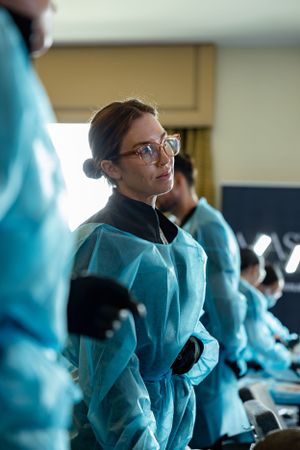Medical professional wearing glasses and teal protective gown smiles during healthcare procedure or training session.