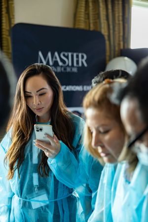 Healthcare professionals in blue PPE check phones during a training session with Master branding visible.