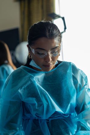 Healthcare worker in blue protective gown and safety glasses focuses during training.