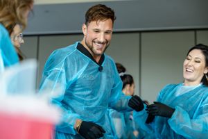 Healthcare workers wearing protective blue gowns and gloves laugh together during a session.