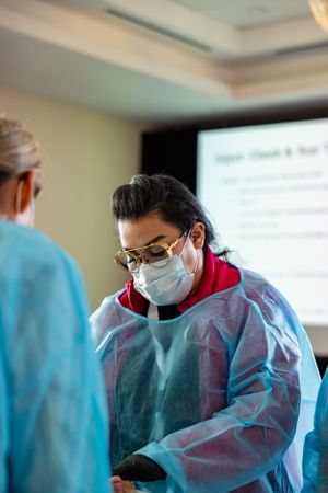 Healthcare worker in protective gear and surgical mask consulting during medical procedure in hospital setting.