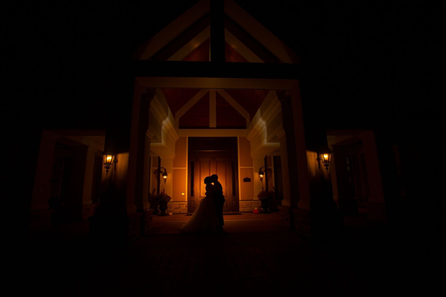 Silhouettes against warm glowing lights in rustic wooden barn venue at night.