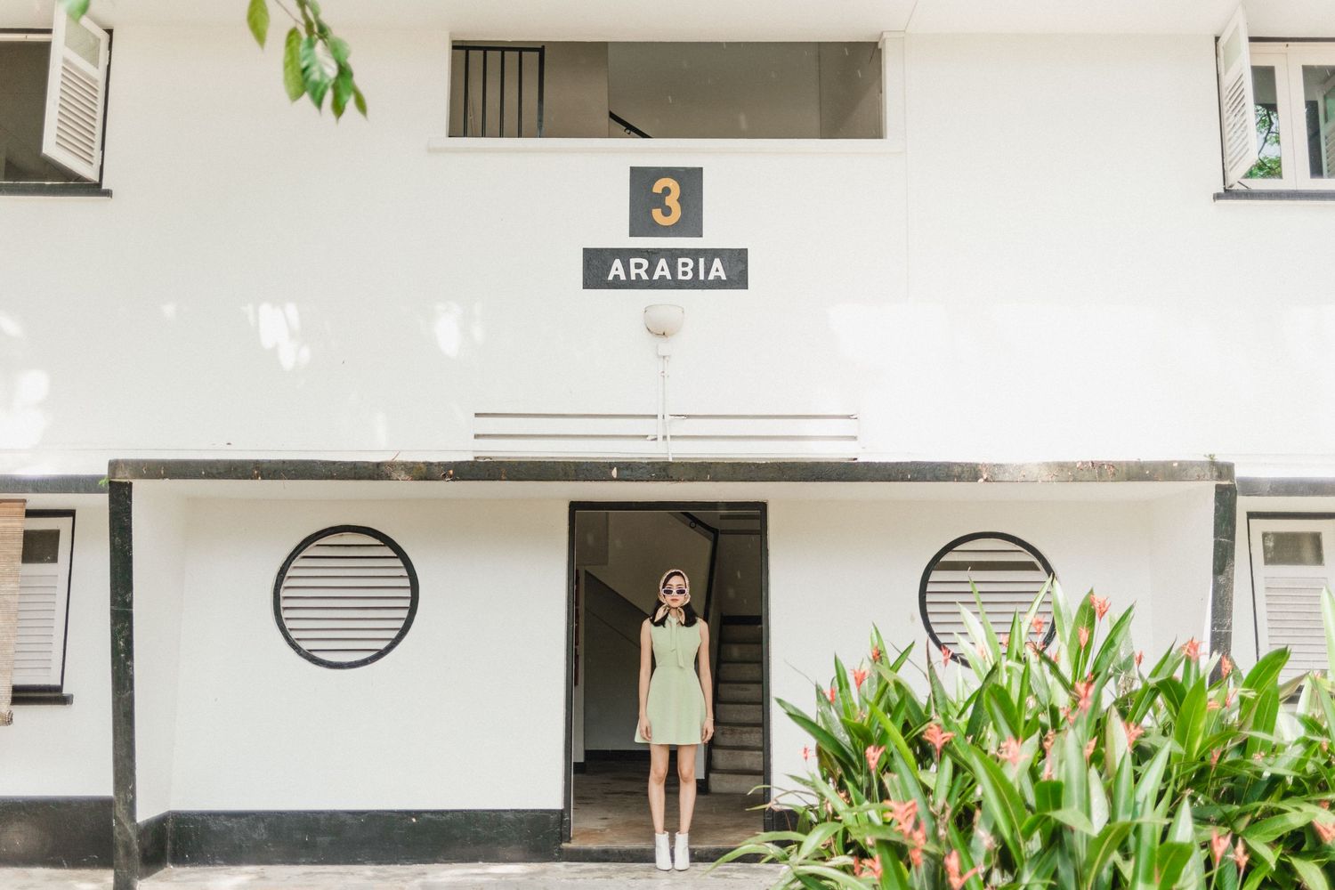 Modern white apartment building exterior with numbered units and tropical landscaping.