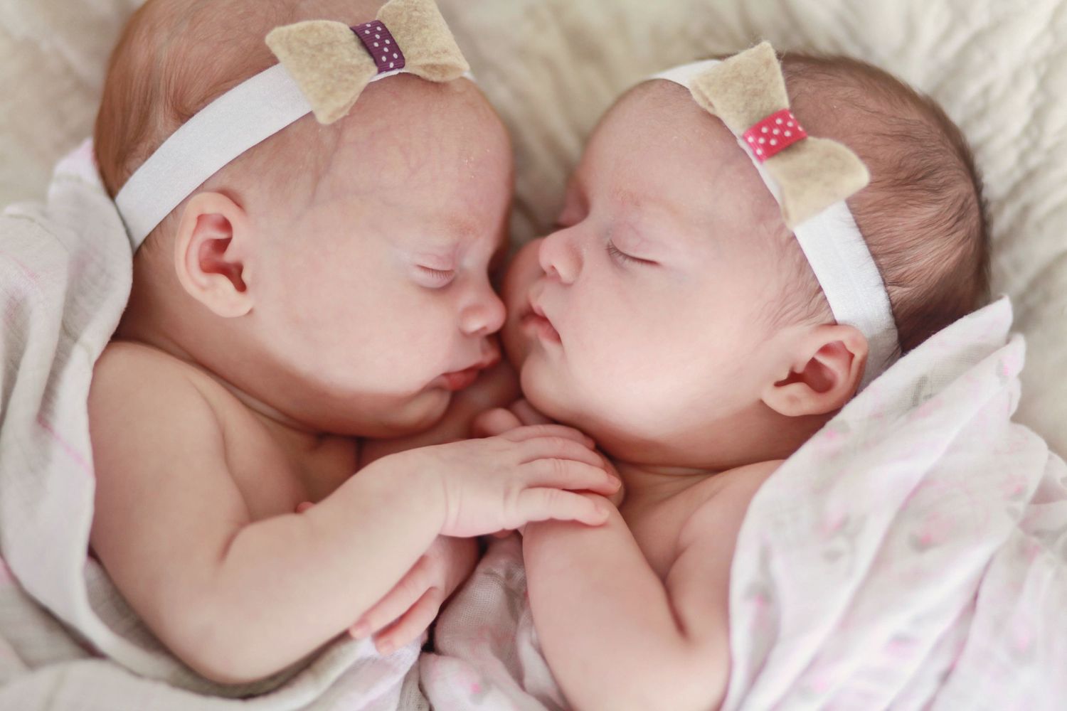 Twin babies sleeping peacefully together wearing matching white headbands.