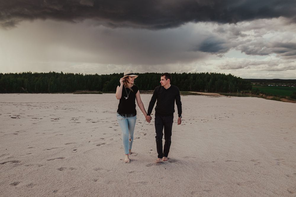 Couple walking along dramatic cloudy beach shoreline.
