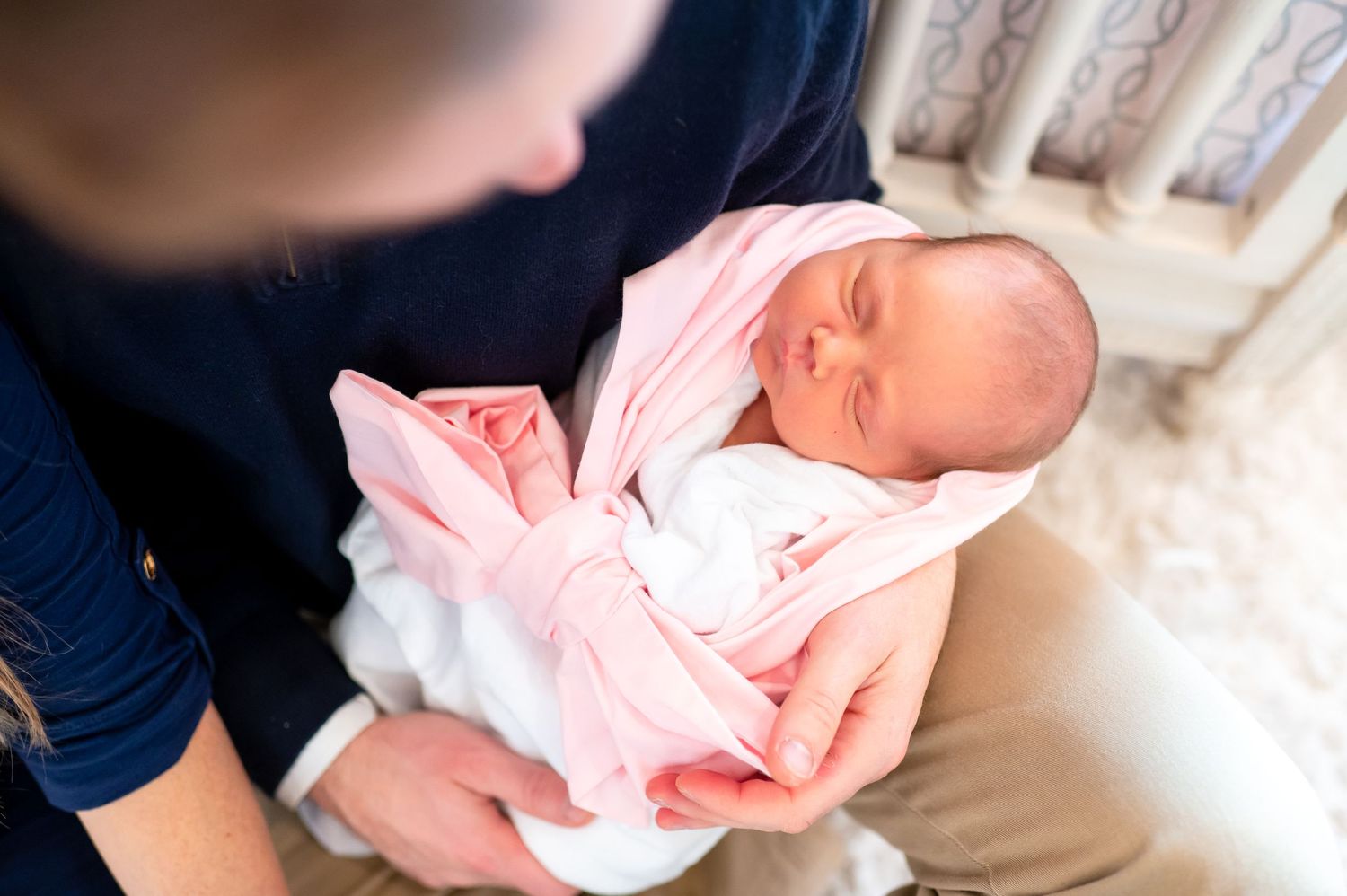 arial shot of a newborn baby girl wrapped in a white blanket and pink bow during a in home newborn lifestyle session