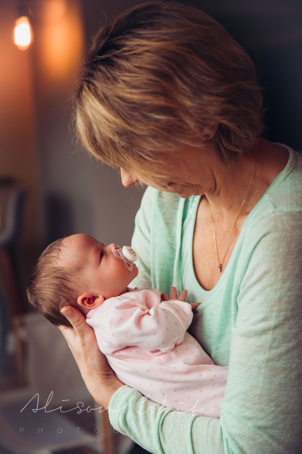 Intimate moment between caregiver in mint sweater holding baby in pink outfit.
