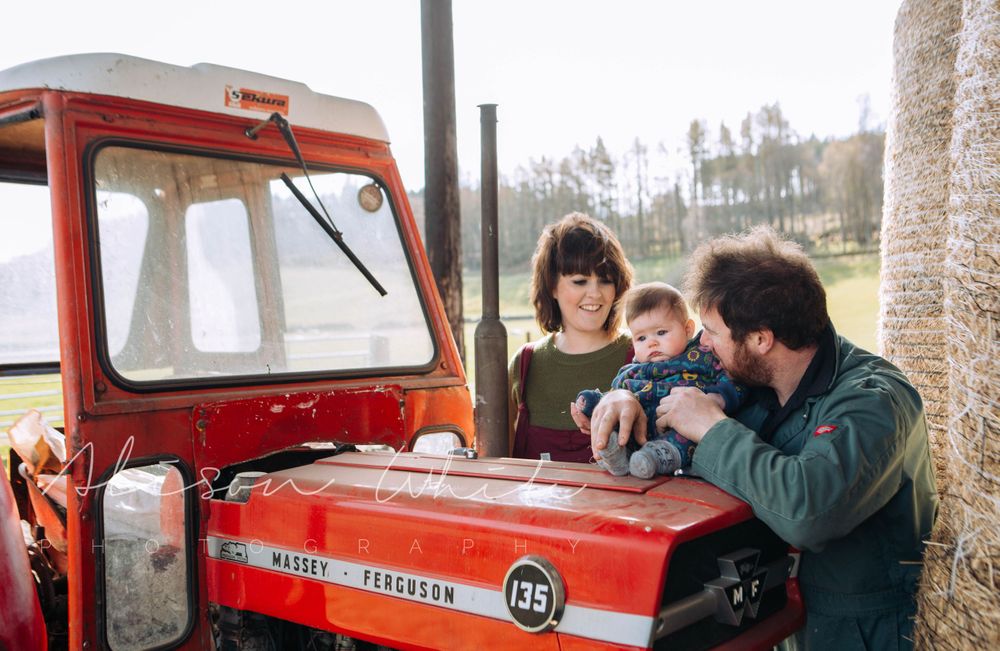 Family gathered around a vintage red tractor on a sunny day at the farm.