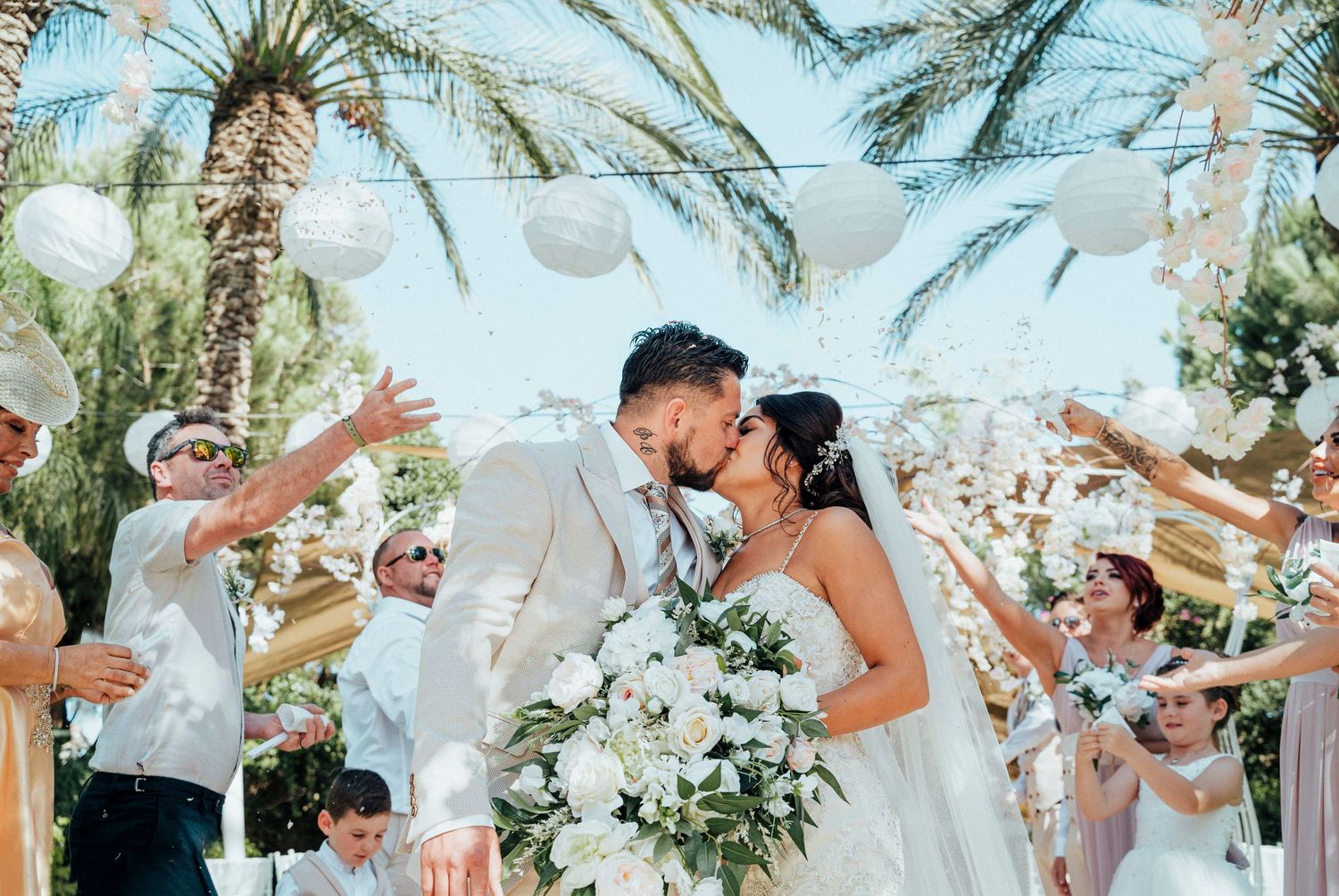 Celebratory wedding ceremony moment under palm trees with guests throwing confetti.