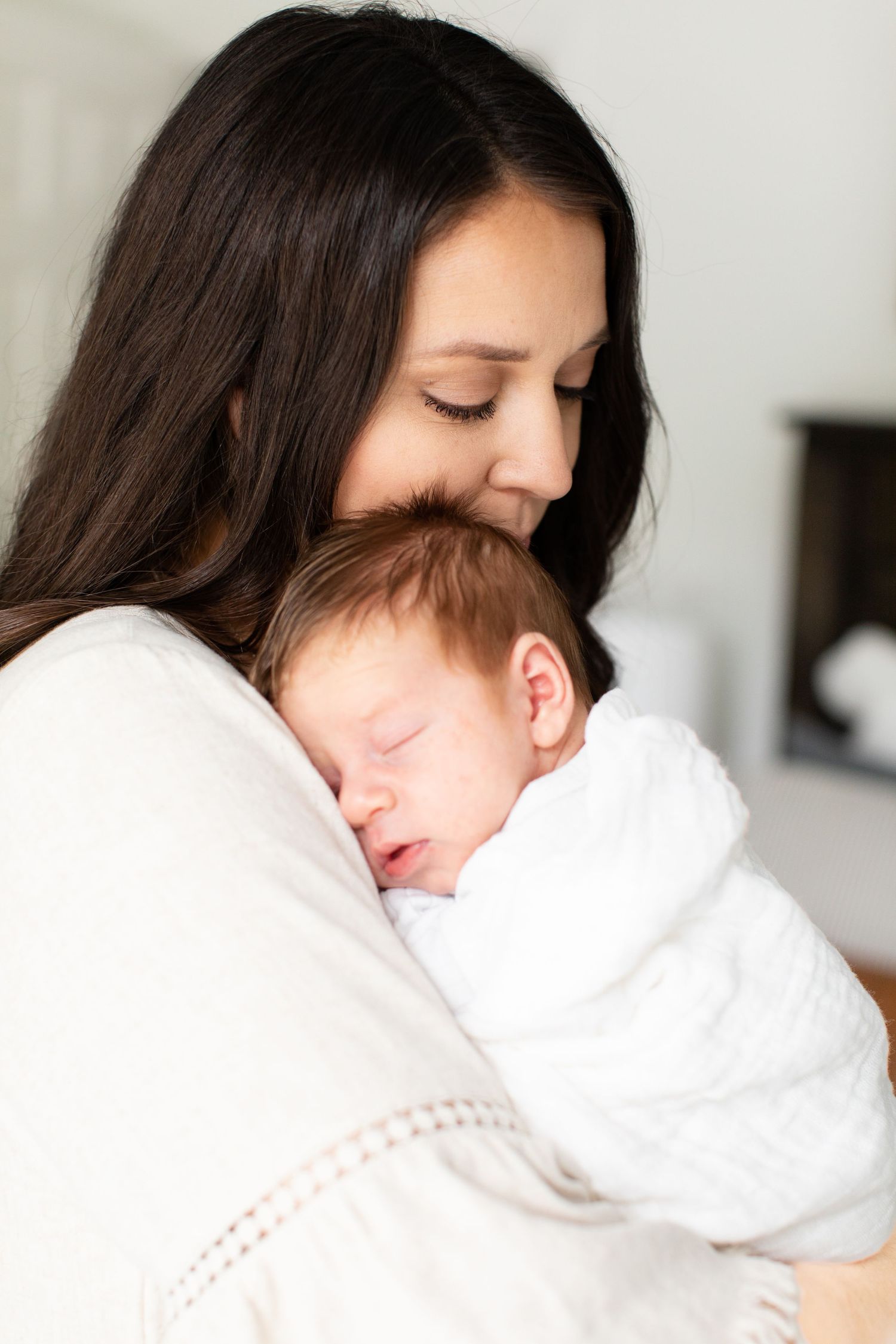 Peaceful moment as sleeping baby rests on parent's shoulder in white nursery setting.