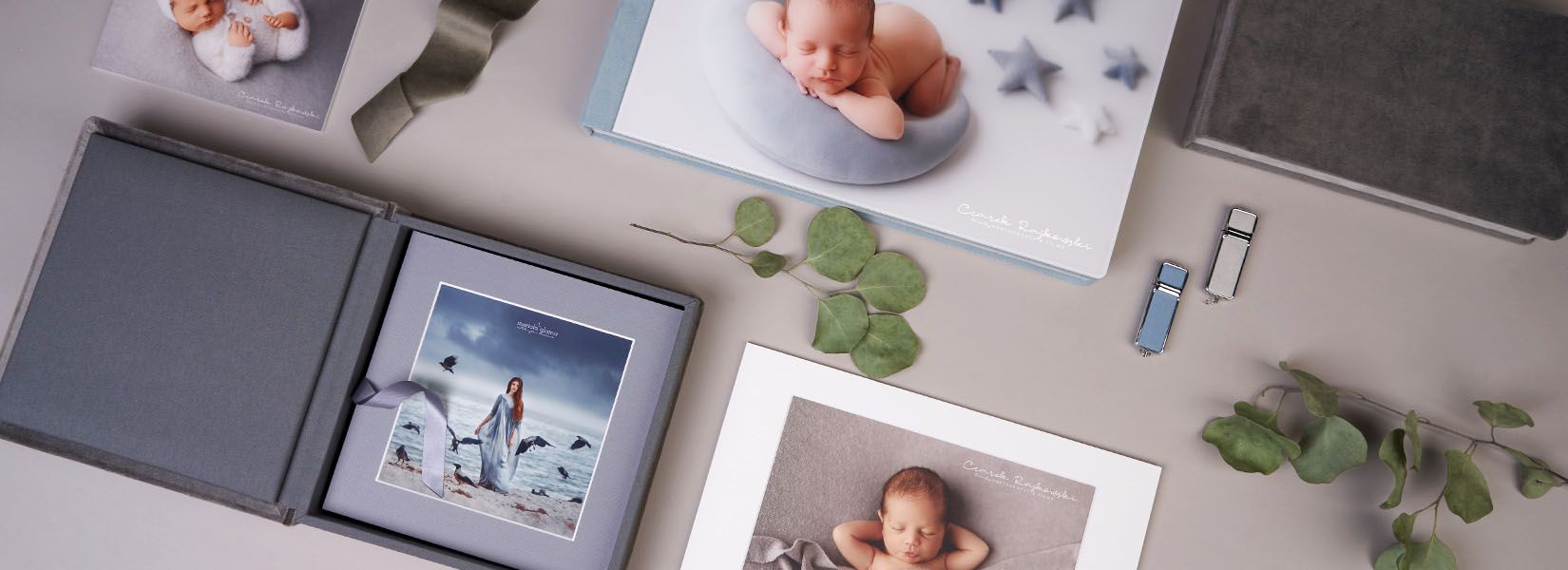 Collection of photo albums and prints arranged with eucalyptus leaves on grey surface.