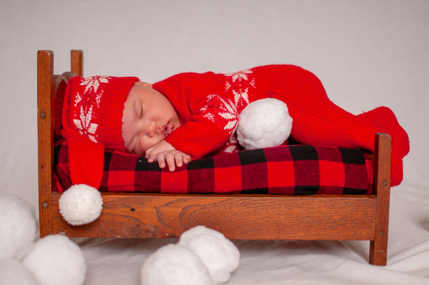 Photo of newborn baby on bed with red plaid blanket and snowballs