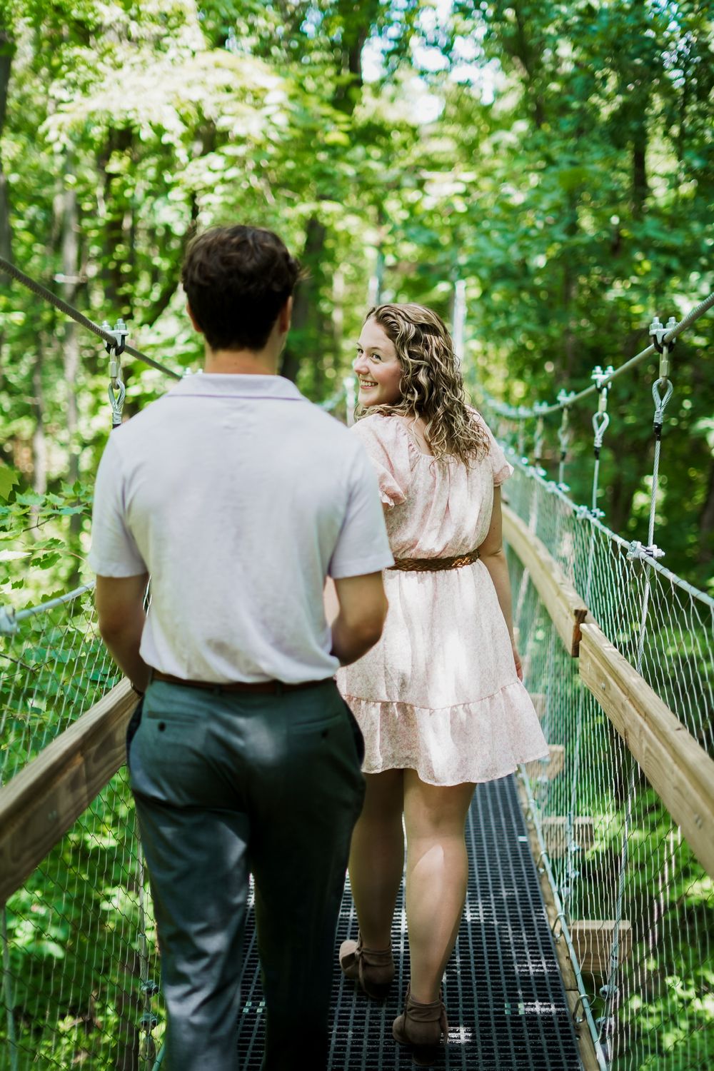 Couple walking together on a wooden bridge path through lush green forest.