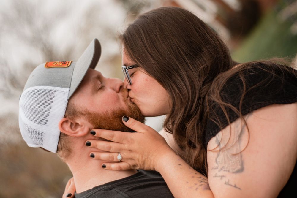 A romantic couple sharing a tender kiss outdoors, with one wearing a white Nike cap.