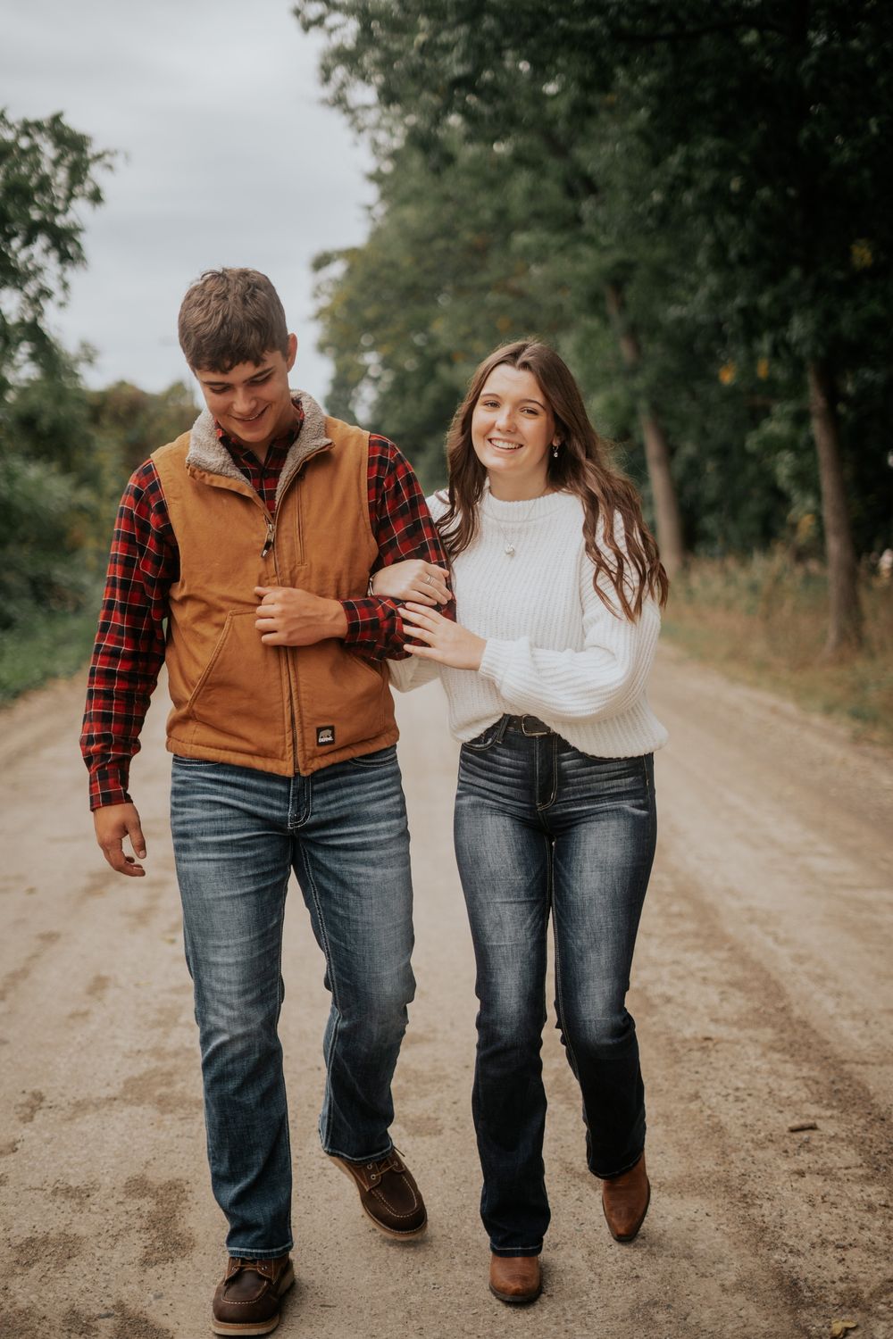A couple walks together on a dirt path wearing casual country attire.