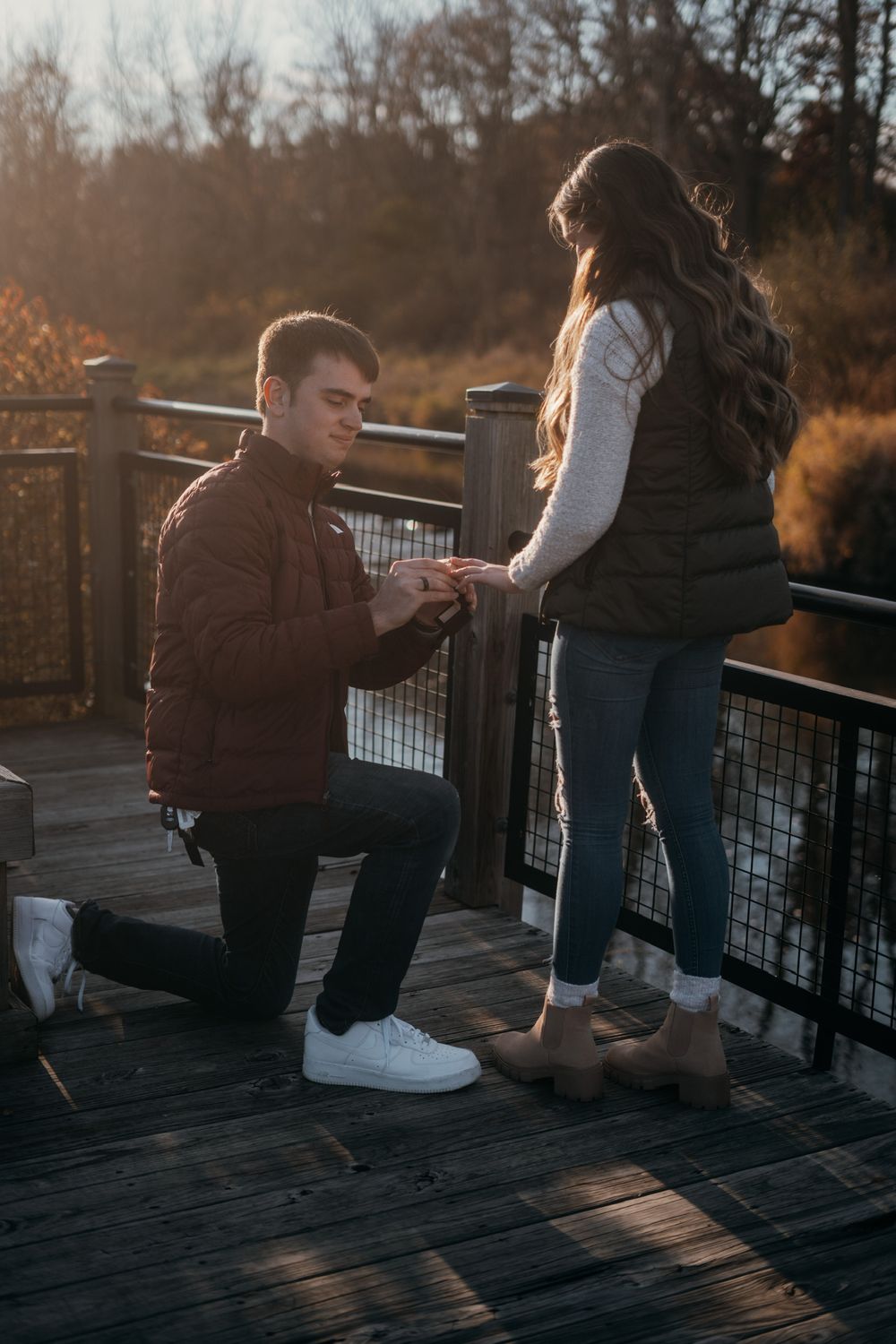 A couple kneels together on a wooden deck during sunset.