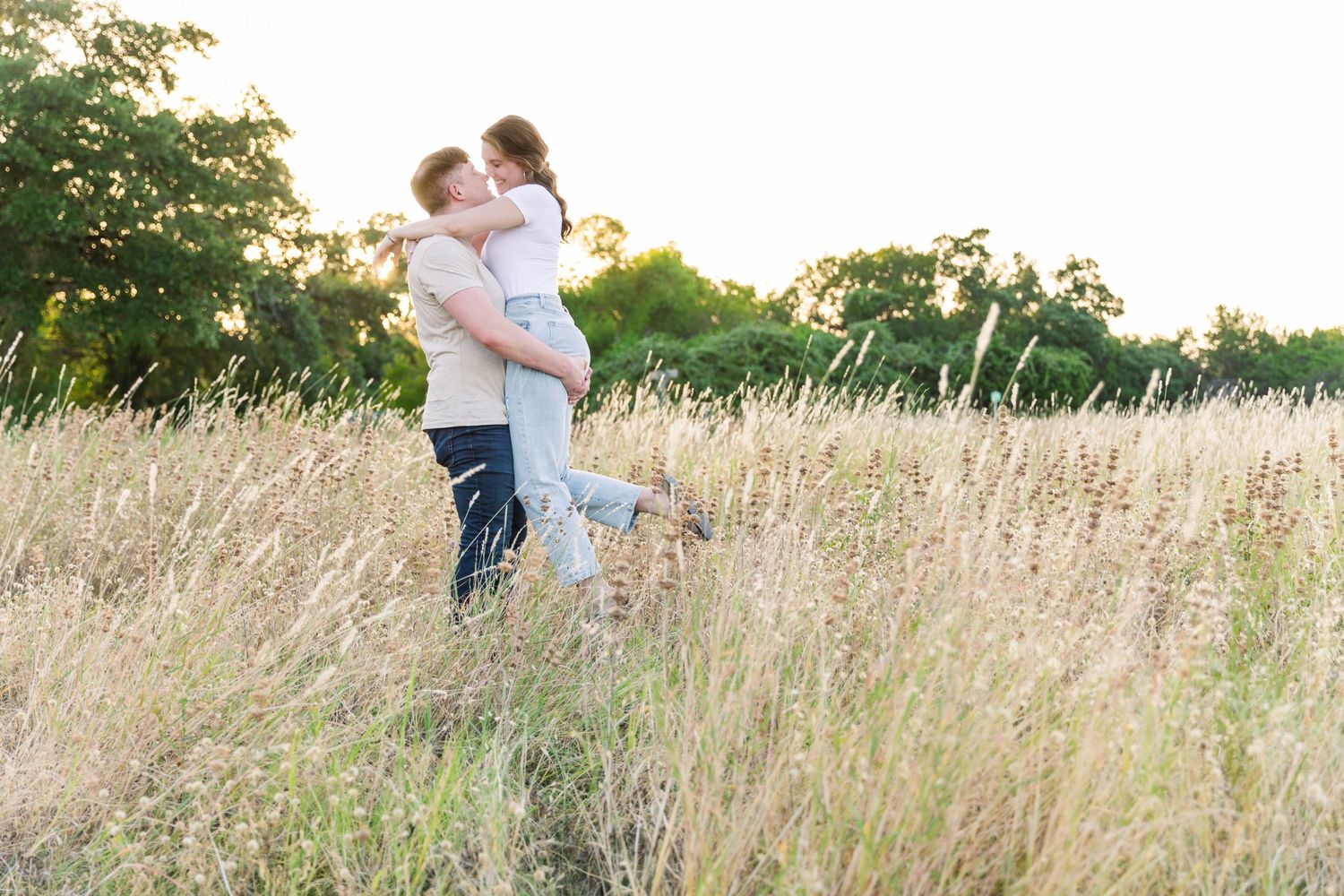 man lifting woman in tall grass field