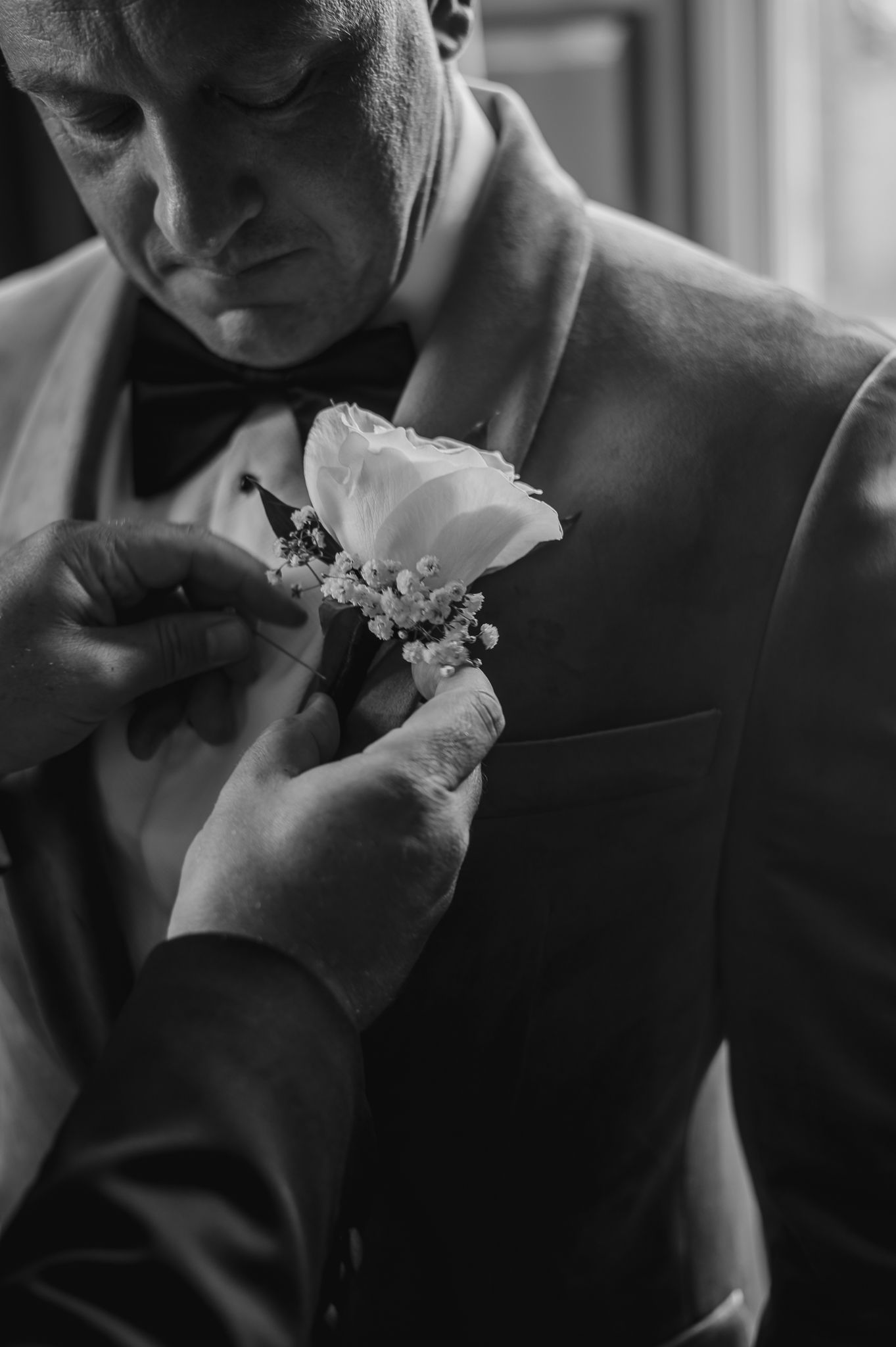 Hands pinning a white rose boutonniere onto a formal suit lapel.