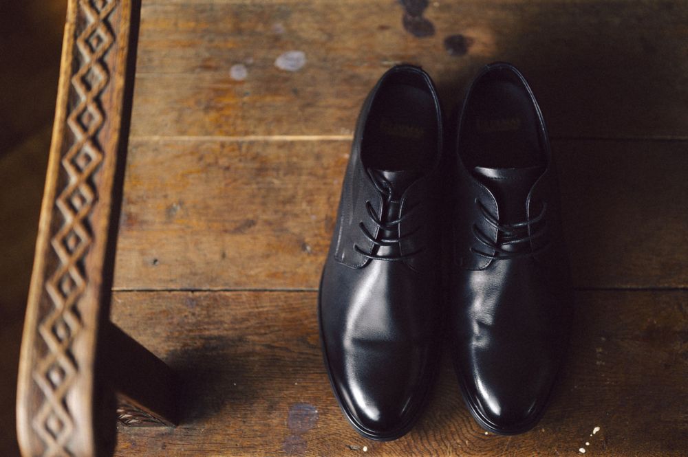 Polished black leather dress shoes on a rustic wooden floor with decorative border.
