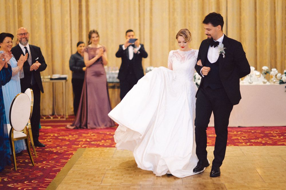 A couple shares their first dance at a reception while guests applaud.