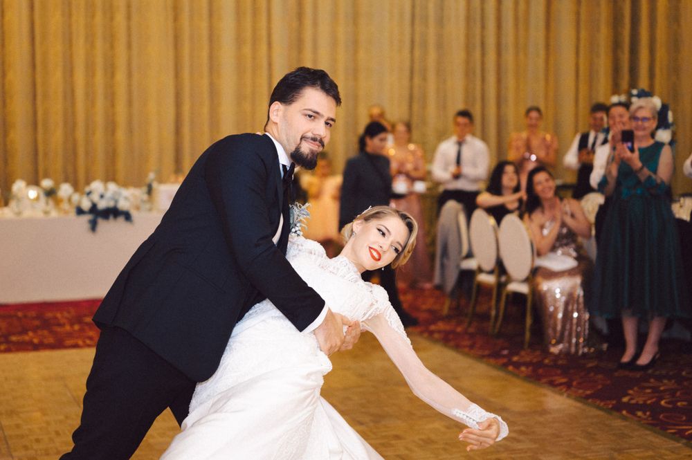 A couple performs a dramatic dip during their first dance at a wedding reception with guests watching in the background.