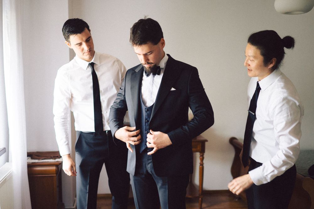Three people in formal attire preparing for an event in a bright room.