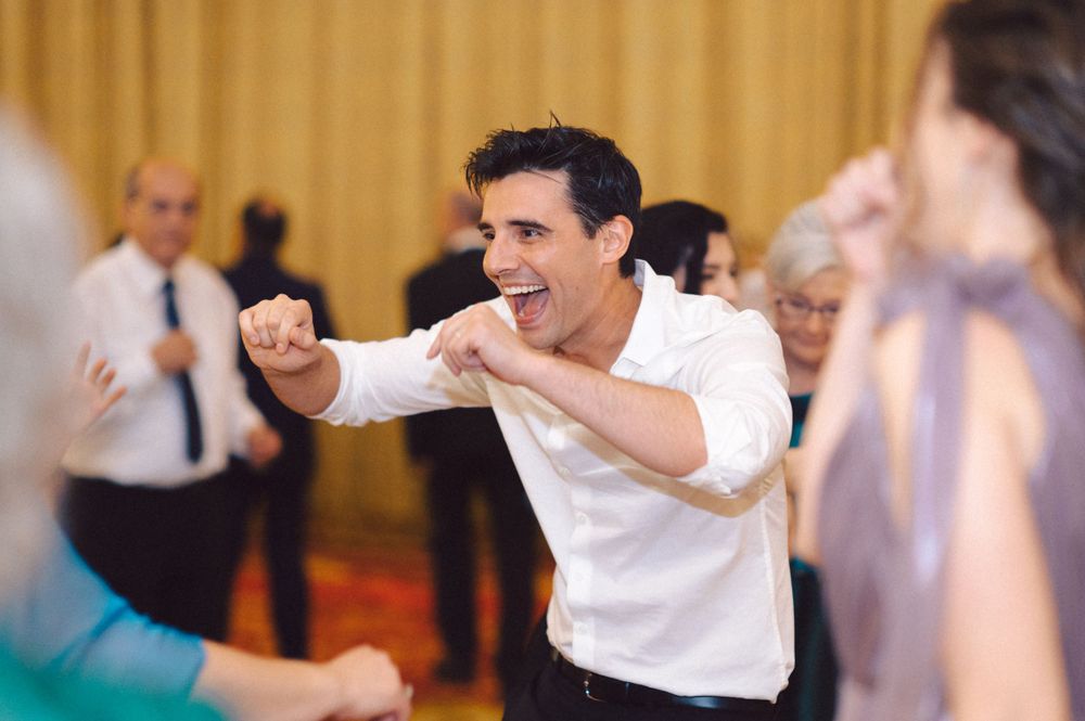 A wedding guest dances energetically in a white shirt on the reception dance floor.