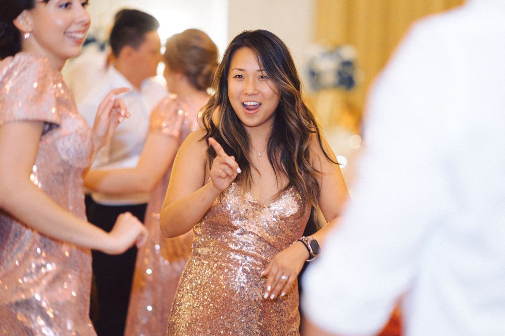 A guest in a sparkly rose gold dress dances joyfully at a wedding reception.