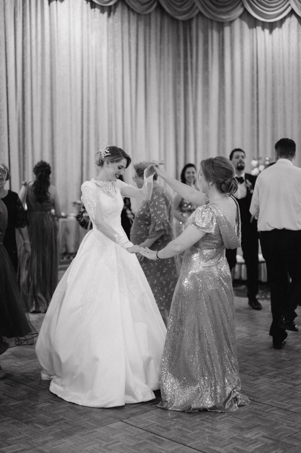 A black and white photo of a bride dancing with a guest in a sequined dress at the reception.