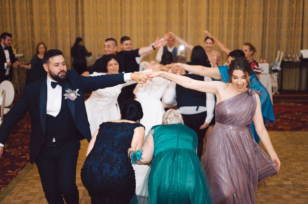 Wedding guests form a circle on the dance floor holding hands in evening attire.